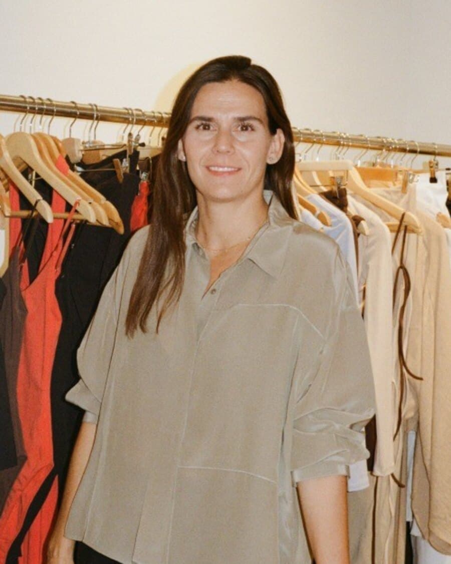 Portrait of Andrea Turell Silva, smiling, in front of a rail of clothes.