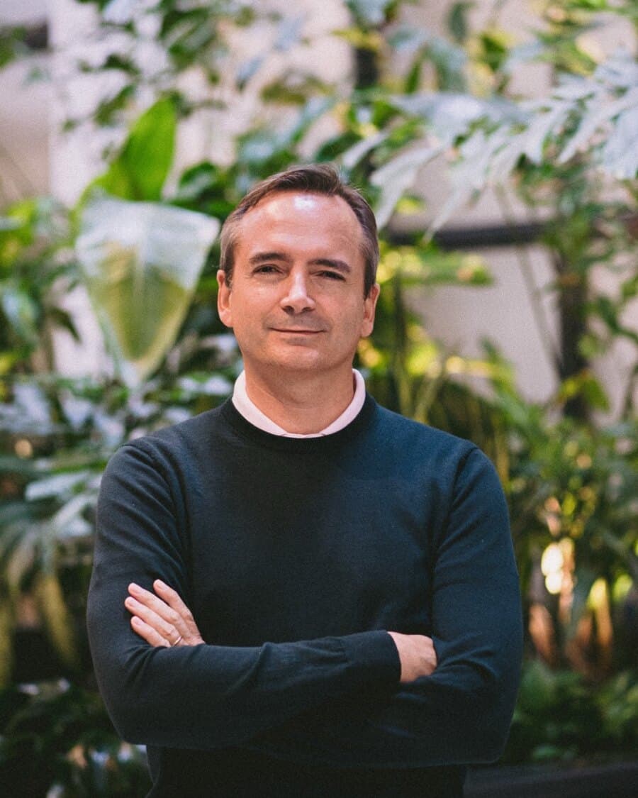 Portrait of Christian Giordano, arms crossed, in front of green plants.
